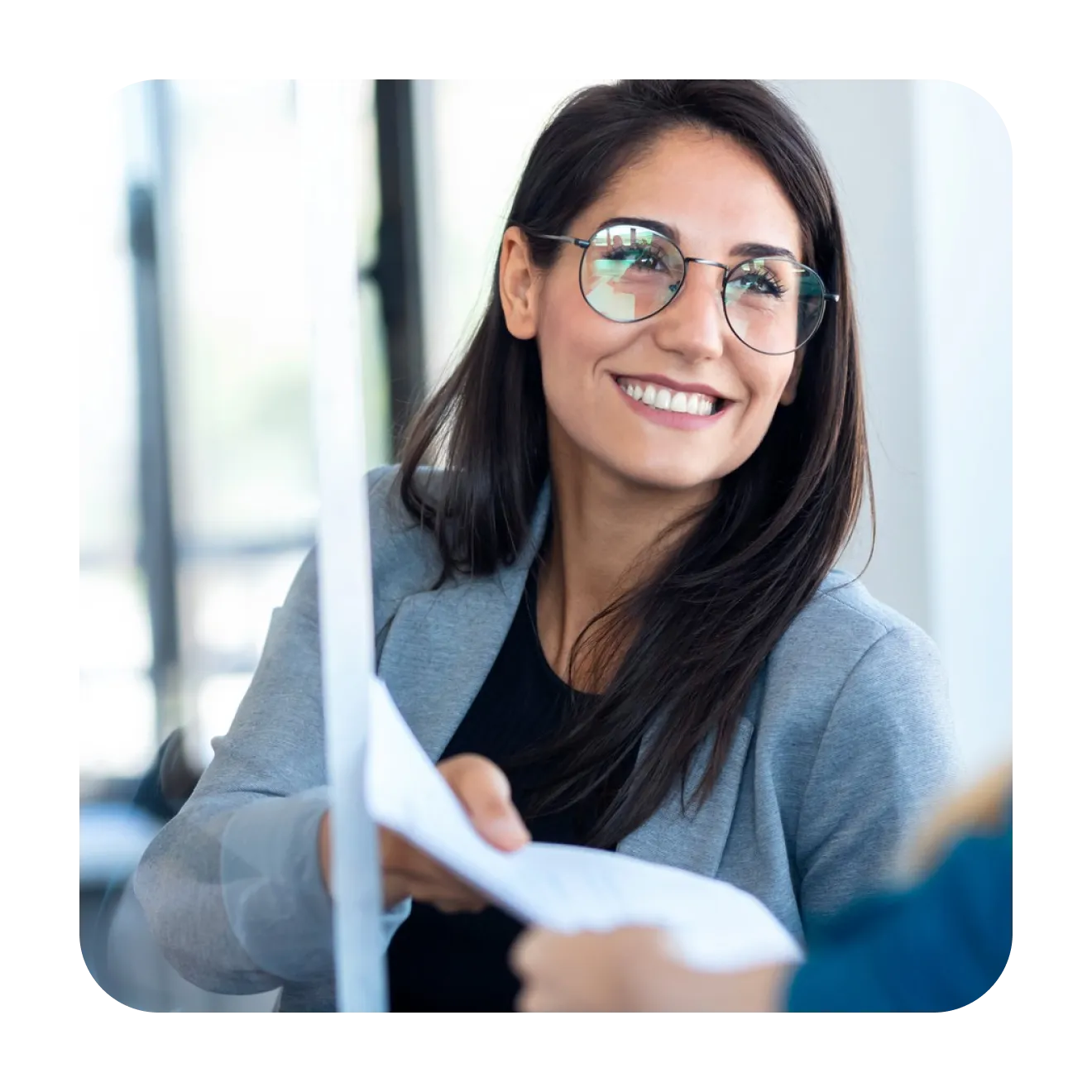Smiling businesswoman in glasses reading a printed report at her desk