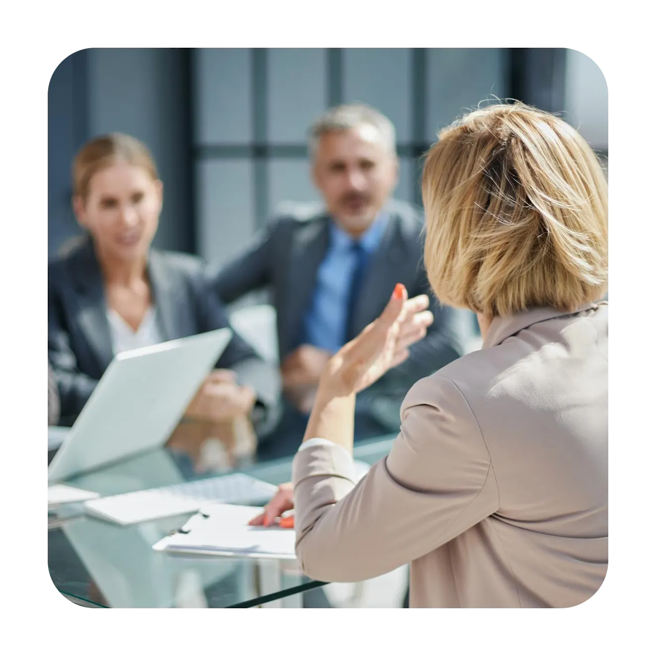 Woman gesturing across a glass meeting table towards two colleagues