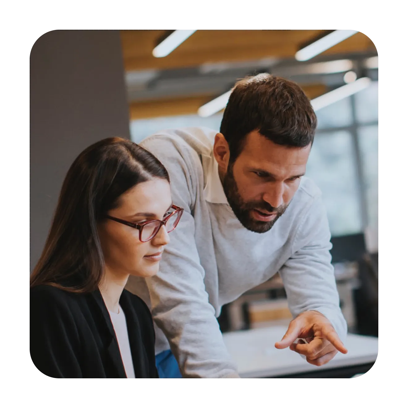 Man leaning over a colleague's desk and pointing at her screen