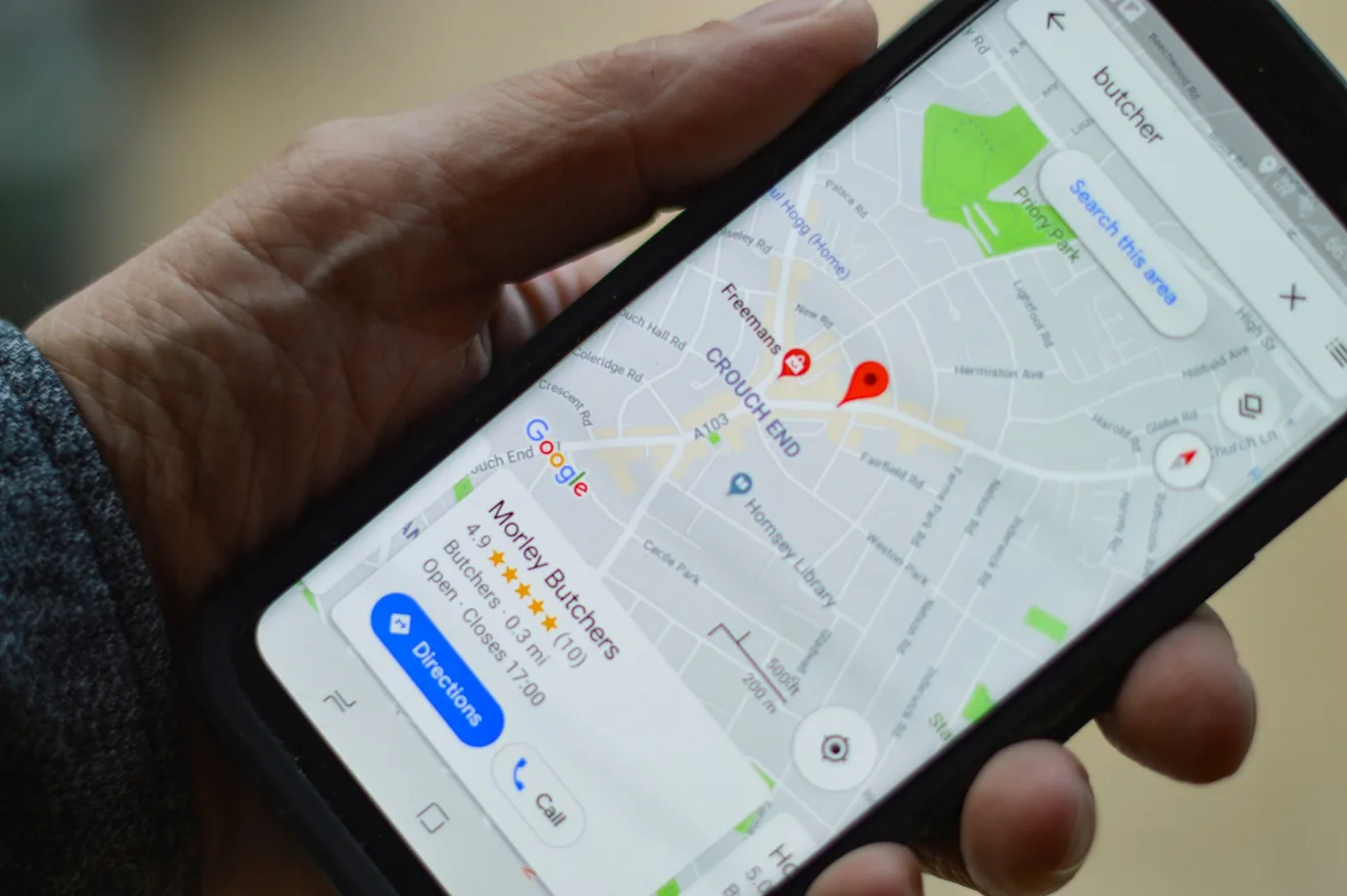 Dłoń trzyma telefon z wizytówką lokalnego sklepu mięsnego w Mapach Google — ocena w gwiazdkach oraz przyciski nawigacji i połączenia.