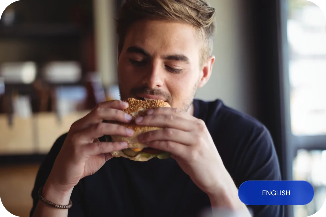 A young man biting into a burger in a fast-food restaurant.