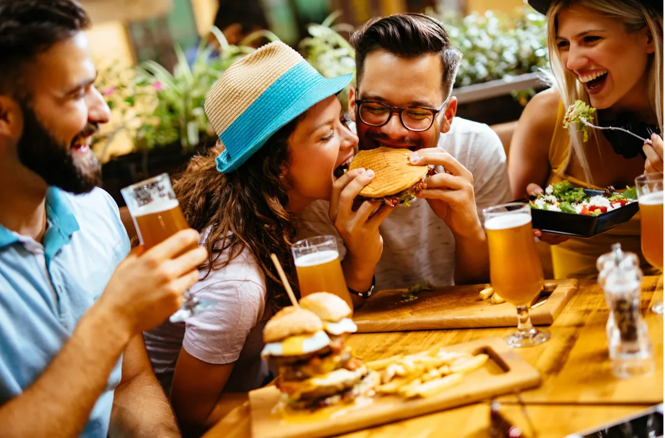 Friends laughing around a restaurant table over burgers, fries and beers.