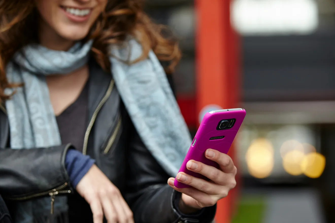 Kobieta w szaliku i skórzanej kurtce uśmiecha się do telefonu w galerii handlowej.